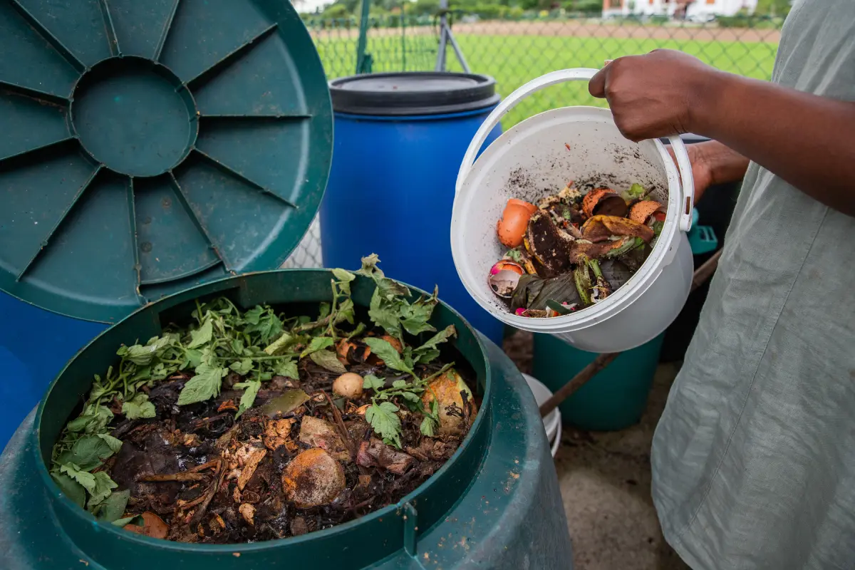 pouring a small composting bin into a large composting pile